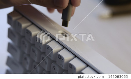 Close-up cable plug connecting into recessed port on white keyboard, showing precise insertion, shallow depth focus, clean workspace details and modern computer interaction Close-up cable plug connecting into recessed port on white keyboard, showing precise insertion, shallow depth focus, clean workspace details and modern computer interaction 142065063