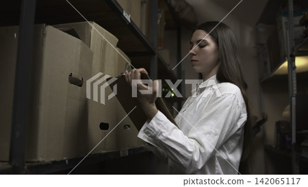 Young woman labeling cardboard boxes in a warehouse aisle Young woman labeling cardboard boxes in a warehouse aisle 142065117