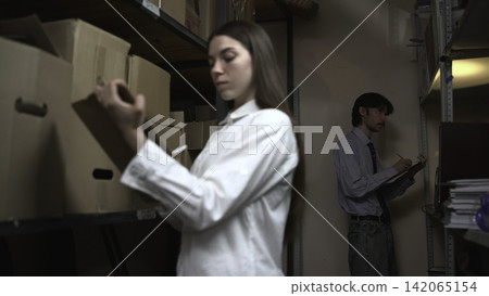 Woman handling box in storage room with man checking inventory Woman handling box in storage room with man checking inventory 142065154