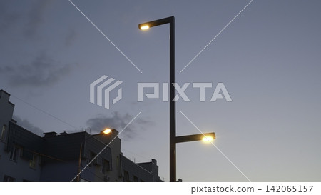 Street lamps glowing over city rooftops at dusk Street lamps glowing over city rooftops at dusk 142065157