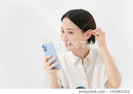 一位女士正透過智慧型手機的前置鏡頭看著自己的臉。 一位女士正透過智慧型手機的前置鏡頭看著自己的臉。 142065261