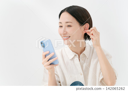 一位女士正透過智慧型手機的前置鏡頭看著自己的臉。 一位女士正透過智慧型手機的前置鏡頭看著自己的臉。 142065262