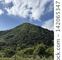 A lush green mountain landscape with a blue sky and clouds. 142065347
