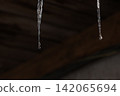 Melting icicles and falling water drops: Close-up of spring thaw on blurred wooden background 142065694
