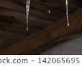 Melting icicles and falling water drops: Close-up of spring thaw on blurred wooden background 142065695