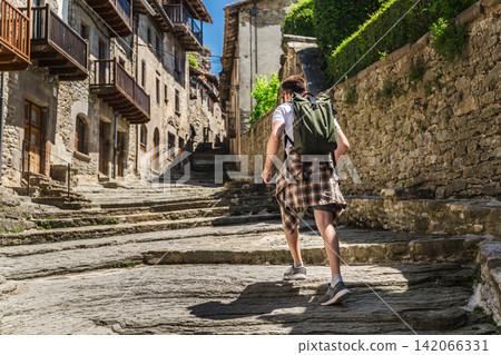 Young male tourist walking along medieval stone street in Rupit village, Catalonia, Spain, exploring historic architecture and authentic Young male tourist walking along medieval stone street in Rupit village, Catalonia, Spain, exploring historic architecture and authentic 142066331