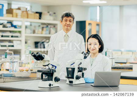 Male and female researchers in white coats conducting research in a laboratory. Male and female researchers in white coats conducting research in a laboratory. 142067139