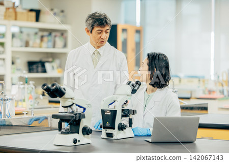 Male and female researchers in white coats conducting research in a laboratory. Male and female researchers in white coats conducting research in a laboratory. 142067143