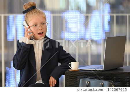 An expressive girl in a business suit and glasses is talking on her smartphone. An expressive girl in a business suit and glasses is talking on her smartphone. 142067615