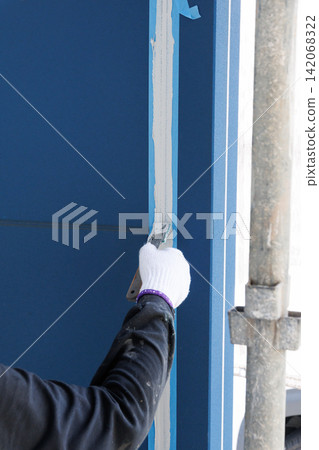 A craftsman's hands smoothing the sealant in the joints of the exterior siding with a spatula. A craftsman's hands smoothing the sealant in the joints of the exterior siding with a spatula. 142068322