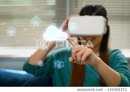 Young Asian Woman Wearing VR Headset Touching Virtual Cloud Computing Icons with Digital Interface Young Asian Woman Wearing VR Headset Touching Virtual Cloud Computing Icons with Digital Interface 142068352