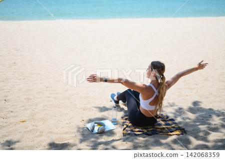 Young woman sitting on the sand with open arms enjoying summer vacation and freedom Young woman sitting on the sand with open arms enjoying summer vacation and freedom 142068359