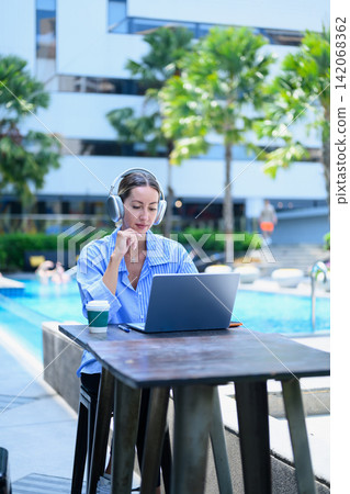 Professional businesswoman working on laptop by the hotel pool during vacation, representing remote work, digital nomad lifestyle 142068362