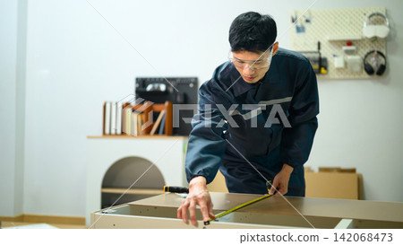 Asian Male Technician in Uniform Measuring Furniture Panel with Tape Measure in Workshop 142068473