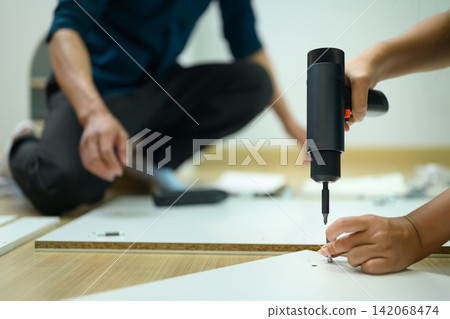 Couple Assembling Flat Pack Furniture Together Using Electric Screwdriver at Home Couple Assembling Flat Pack Furniture Together Using Electric Screwdriver at Home 142068474
