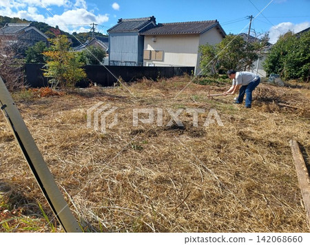 秋天,在剛割過的枯草叢中,一個穿著短袖襯衫的男人正在耕作一片破敗的農田,遠處可以看到日本的鄉村住宅區。 秋天,在剛割過的枯草叢中,一個穿著短袖襯衫的男人正在耕作一片破敗的農田,遠處可以看到日本的鄉村住宅區。 142068660