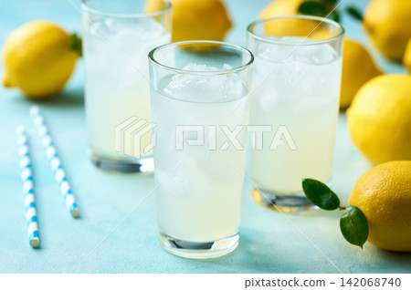 Glasses of freshly made lemonade on turquoise background, selective focus. Glasses of freshly made lemonade on turquoise background, selective focus. 142068740