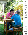 A woman and child engaging in creative activities outside, painting and drawing in a sunny, natural garden setting, promoting artistry. 142069146