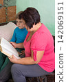 Grandmother and grandson share a moment reading together indoors, fostering learning and connection in a cozy setting. 142069151