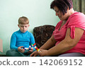 Grandmother and grandson spend time together. They are sitting and playing together on the floor with plastic interlocking toy blocks. 142069152