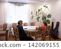 Grandmother and child sit at a table indoors, spending time together. A potted plant is nearby. Calm, family, togetherness, inside. 142069155
