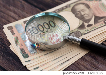 10萬日圓面額的1萬日元鈔票和一個放大鏡 10萬日圓面額的1萬日元鈔票和一個放大鏡 142069172