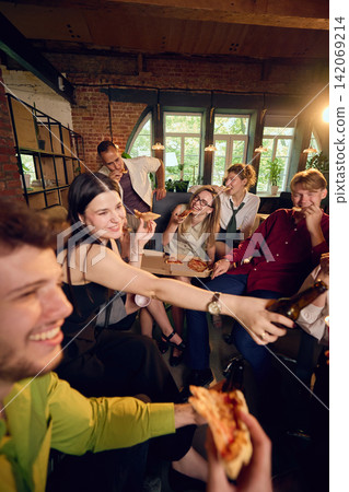 Coworker passing pizza slice across crowded office party table Coworker passing pizza slice across crowded office party table 142069214