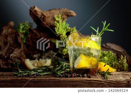Gin and tonic cocktail with ice, lemon, juniper berries and rosemary sprigs sits on an old weathered board. Gin and tonic cocktail with ice, lemon, juniper berries and rosemary sprigs sits on an old weathered board. 142069324