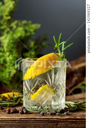 Gin and tonic cocktail with ice, lemon, juniper berries and rosemary sprigs sits on an old weathered board. Gin and tonic cocktail with ice, lemon, juniper berries and rosemary sprigs sits on an old weathered board. 142069327