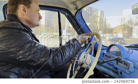 Male driver riding on blue vintage auto at city road on sunny day. Serious man driving retro vehicle at urban street. Confident guy moving in his old auto on route. Slow motion Male driver riding on blue vintage auto at city road on sunny day. Serious man driving retro vehicle at urban street. Confident guy moving in his old auto on route. Slow motion 142069736