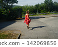 Girl Joyfully Running in a Red Dress on Sunny Street 142069856