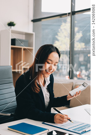 Asian businesswoman using calculator and working on laptop at modern office Asian businesswoman using calculator and working on laptop at modern office 142069868