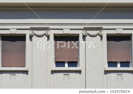 Windows with pulled down roller shutters on white classic facade Windows with pulled down roller shutters on white classic facade 142070024
