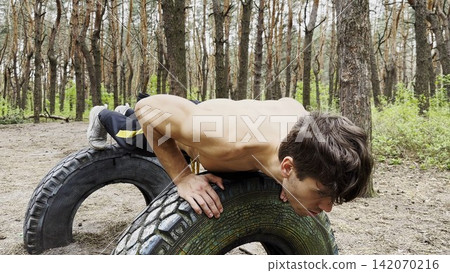Strong sporty man doing push ups at summer forest. Young muscular athlete working out at woodland. Male shirtless athlete training at nature. Concept of active and healthy lifestyle. Slow motion Strong sporty man doing push ups at summer forest. Young muscular athlete working out at woodland. Male shirtless athlete training at nature. Concept of active and healthy lifestyle. Slow motion 142070216
