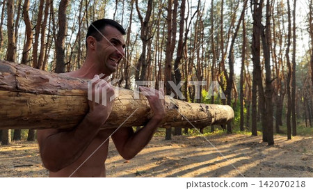 Hardy shirtless sportsman lifting wooden log at summer forest. Young athletic guy exercises with hard weight training biceps. Strong muscular man working at sunny woodland. Active lifestyle concept Hardy shirtless sportsman lifting wooden log at summer forest. Young athletic guy exercises with hard weight training biceps. Strong muscular man working at sunny woodland. Active lifestyle concept 142070218