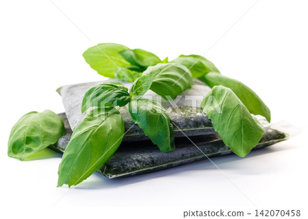 Fresh basil leaves arranged with frozen herb packages on white background Fresh basil leaves arranged with frozen herb packages on white background 142070458