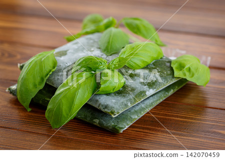 Vacuum sealed frozen basil with fresh leaves on wooden table Vacuum sealed frozen basil with fresh leaves on wooden table 142070459