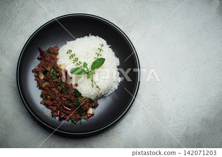 home made Thai's style spicy stir fried basil with minced beef served with Thai jasmine rice in black dish put on naked gray concrete texture dinner table with small free copy space on a side 142071203