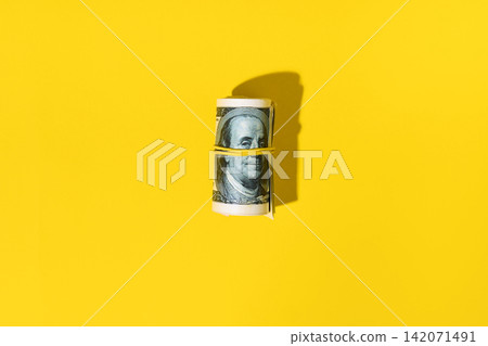 Roll of hundred dollar bills on yellow background Roll of hundred dollar bills on yellow background 142071491