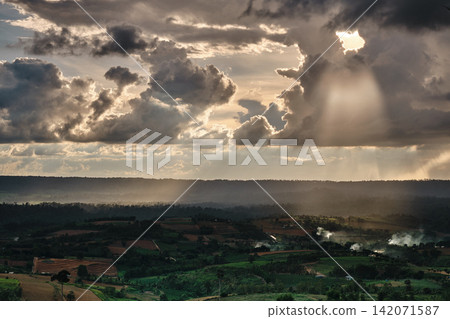 Sunset over the mountains in cloudy sky with sun rays down to the hills with green forest and agricultural field Sunset over the mountains in cloudy sky with sun rays down to the hills with green forest and agricultural field 142071587