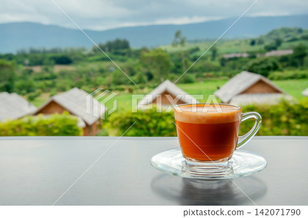 hot Thai's style milk tea in a cup with mountain view when a raining is coming from somewhere faraway hot Thai's style milk tea in a cup with mountain view when a raining is coming from somewhere faraway 142071790