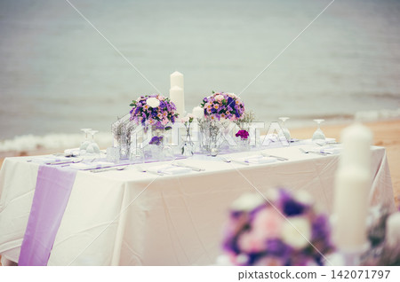 romantic wedding reception party's dinner table with a bouquets on the beach and blue sea in background in the afternoon romantic wedding reception party's dinner table with a bouquets on the beach and blue sea in background in the afternoon 142071797