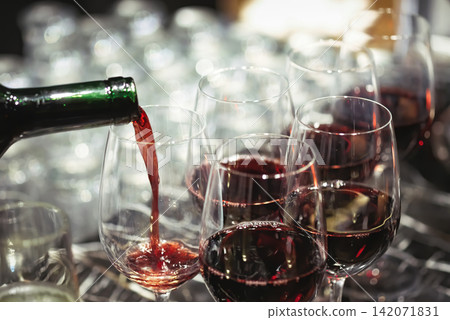 pouring wine in many glasses for dinner party, shot with narrow focus. pouring wine in many glasses for dinner party, shot with narrow focus. 142071831