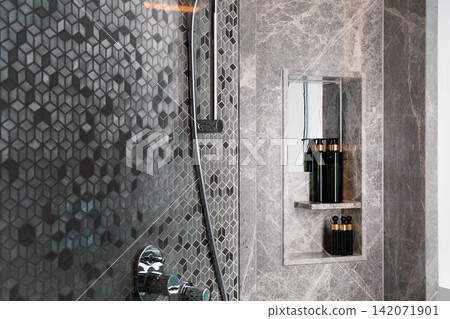 The bottles of shampoo and soap are on the shelf in the wall next to the shower in the bathroom with beautiful wallpaper. 142071901