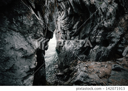 A shot of a big frame of rusty weathered fabric caught on coastal rocky cliff with a small space of sea A shot of a big frame of rusty weathered fabric caught on coastal rocky cliff with a small space of sea 142071913