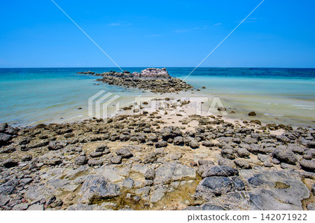 rocky shore and a sandy beach on the island with blue-green sea and clear blue sky 142071922