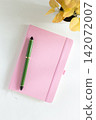 Pink notebook cover with green pen and yellow leaves plant on white desk 142072007
