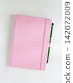 Pink notebook with green pen tucked in elastic band, top view 142072009