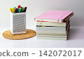 Stacked Books with pink Notebook on top and markers on Desk 142072017
