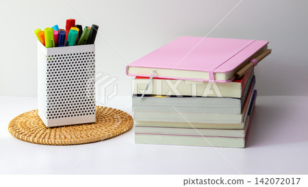 Stacked Books with pink Notebook on top and markers on Desk Stacked Books with pink Notebook on top and markers on Desk 142072017